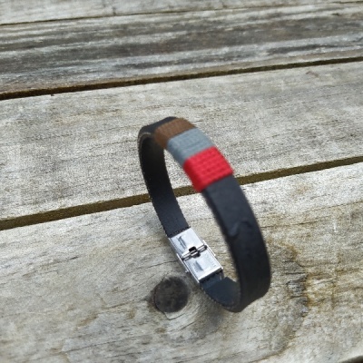 Pulseira de couro preta com detalhes coloridos e fecho metálico sobre madeira