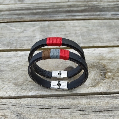 Dois pulseiras de couro preto com detalhes em fios coloridos e fecho metálico sobre madeira clara