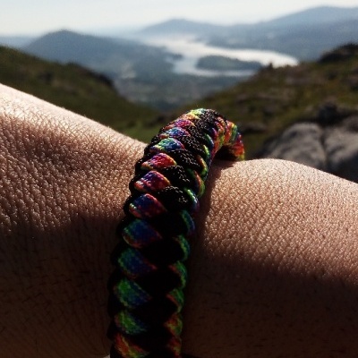 Pulseira trançada colorida num pulso com montanhas ao fundo