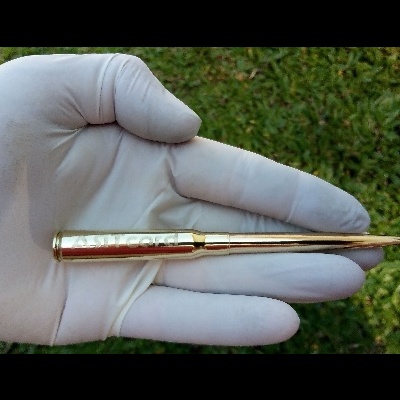 Munição metálica dourada segurada por mão com luva branca sobre relva verde