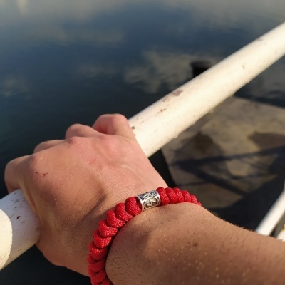 Pulseira vermelha trançada com fecho metálico num pulso masculino junto a água