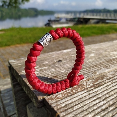 Pulseira trançada vermelha com fecho de metal sobre madeira ao ar livre