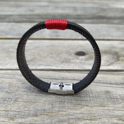 Pulseira em pele preta com costura castanha e detalhe vermelho sobre madeira