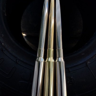 Três estojos de munição longos metálicos em prata e dourado sobre pneu preto.