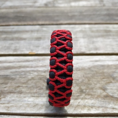 Pulseira entrelaçada vermelha e preta sobre madeira clara