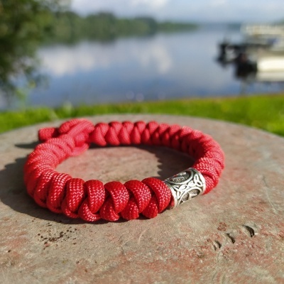 Pulseira vermelha entrelaçada com detalhe metálico prateado sobre pedra ao ar livre