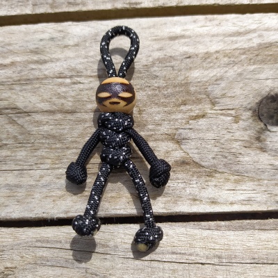 Figura humana feita de corda preta com cabeça de madeira pintada sobre madeira rústica