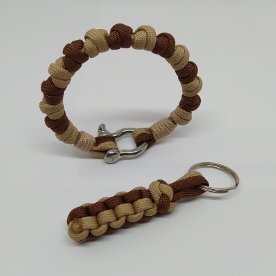 Pulseira e porta-chaves trançados castanho claro e castanho escuro com detalhes metálicos prateados no fundo branco