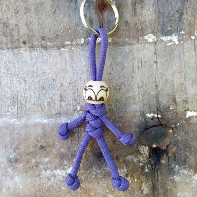 Chaveiro de boneco de corda roxa com cabeça de madeira e olhos desenhados