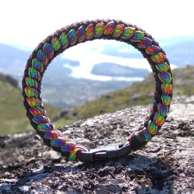 Pulseira trançada colorida com fecho preto sobre rocha em paisagem montanhosa