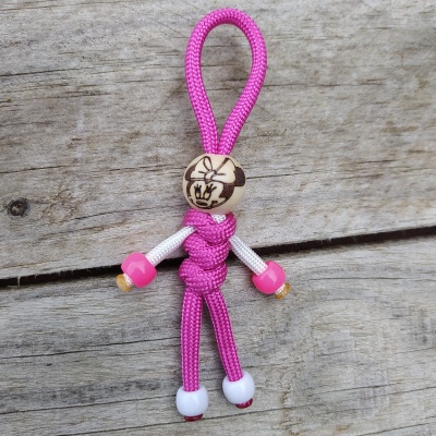 Chaveiro boneco em corda rosa e branca com cabeça de conta de madeira desenhada sobre madeira.