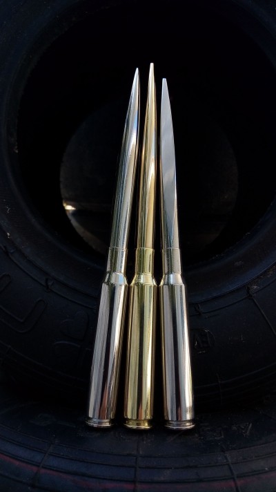 Três estojos de munição longos metálicos em prata e dourado sobre pneu preto.