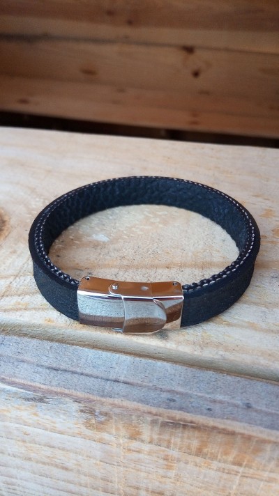 Pulseira preta de couro com fecho metálico prateado sobre superfície de madeira