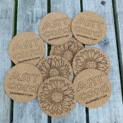 Bases redondas de cortiça com padrões de girassol e texto ART cord HANDMADE STUFF sobre madeira envelhecida.