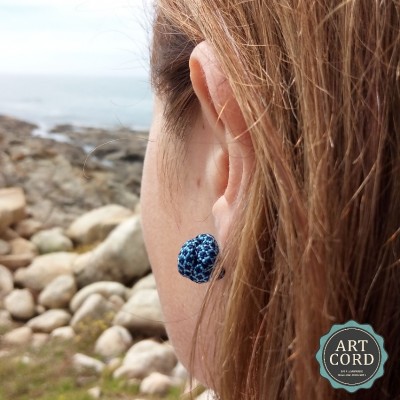 Brinco bola textura azul na orelha com fundo de pedras e mar