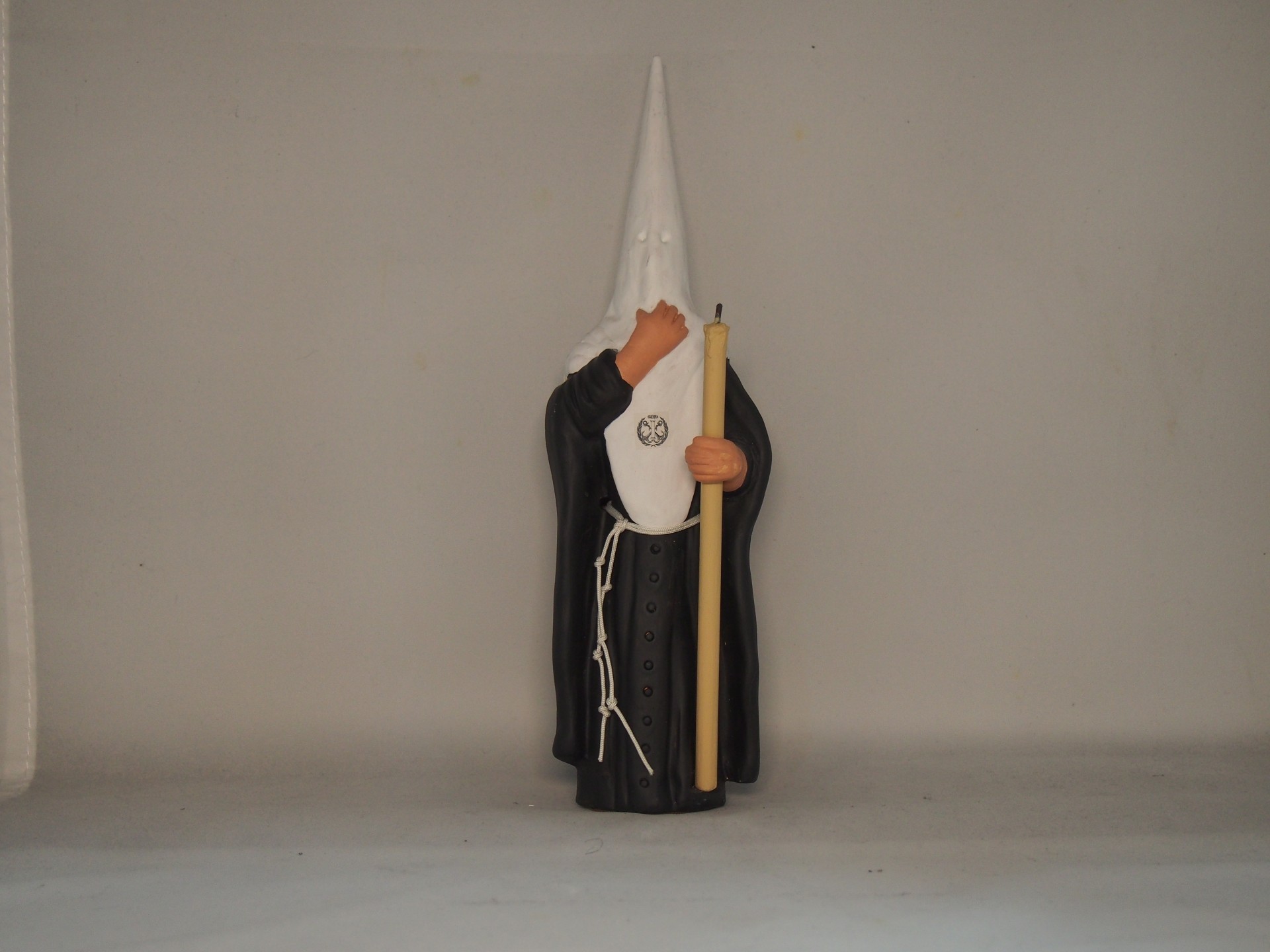 Estatueta de nazareno com túnica preta e capuz branco segurando vela