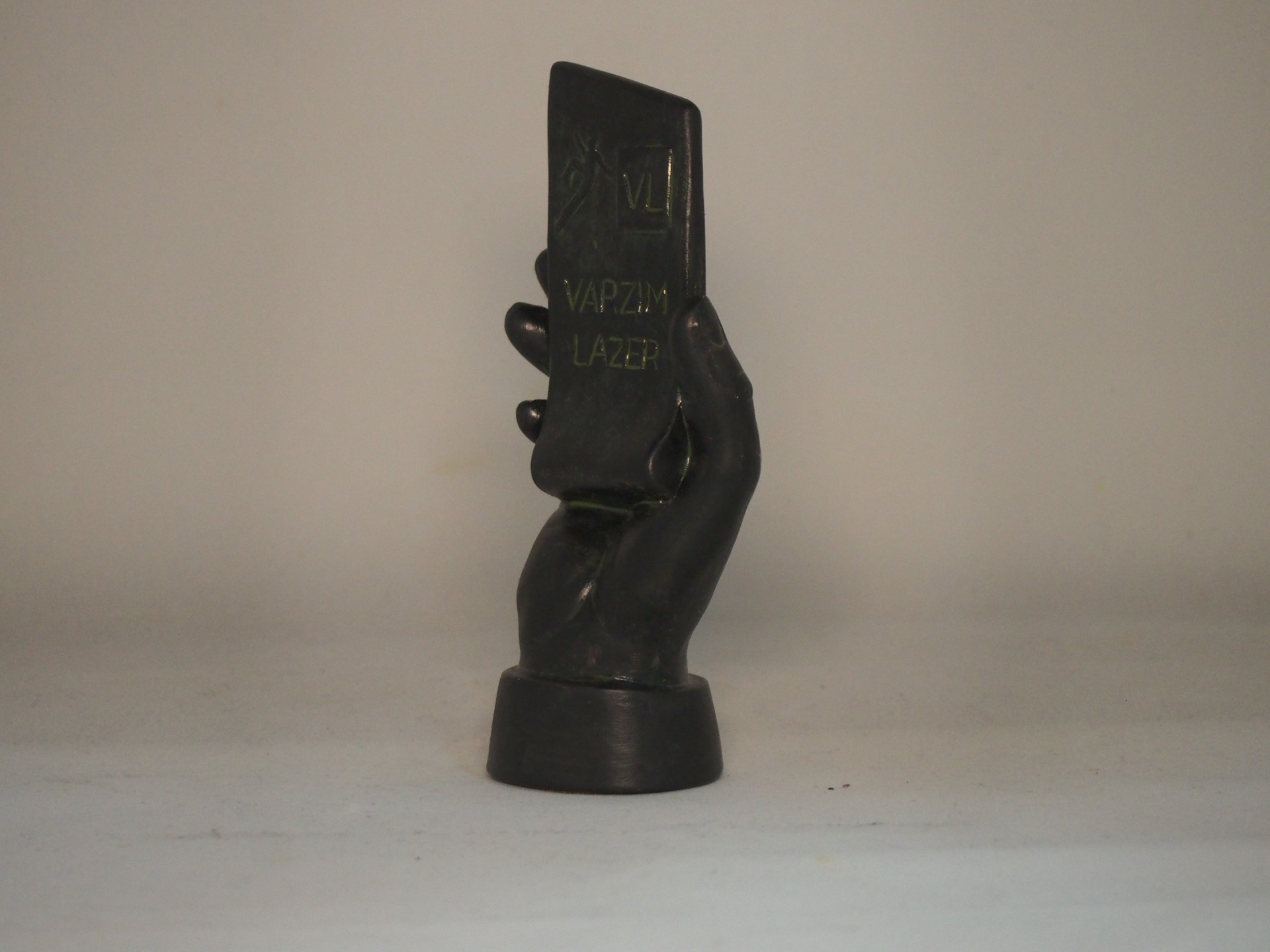 Escultura preta de uma mão segurando objeto retangular com texto VIPZILIA LAZER