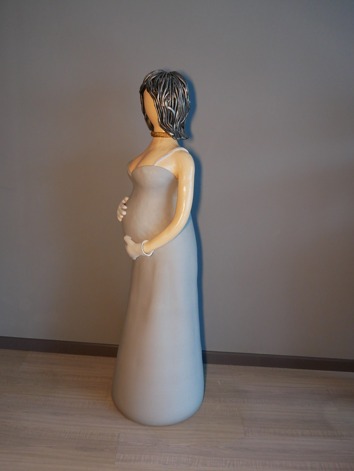 Estátua de mulher grávida com vestido cinzento e cabelo castanho