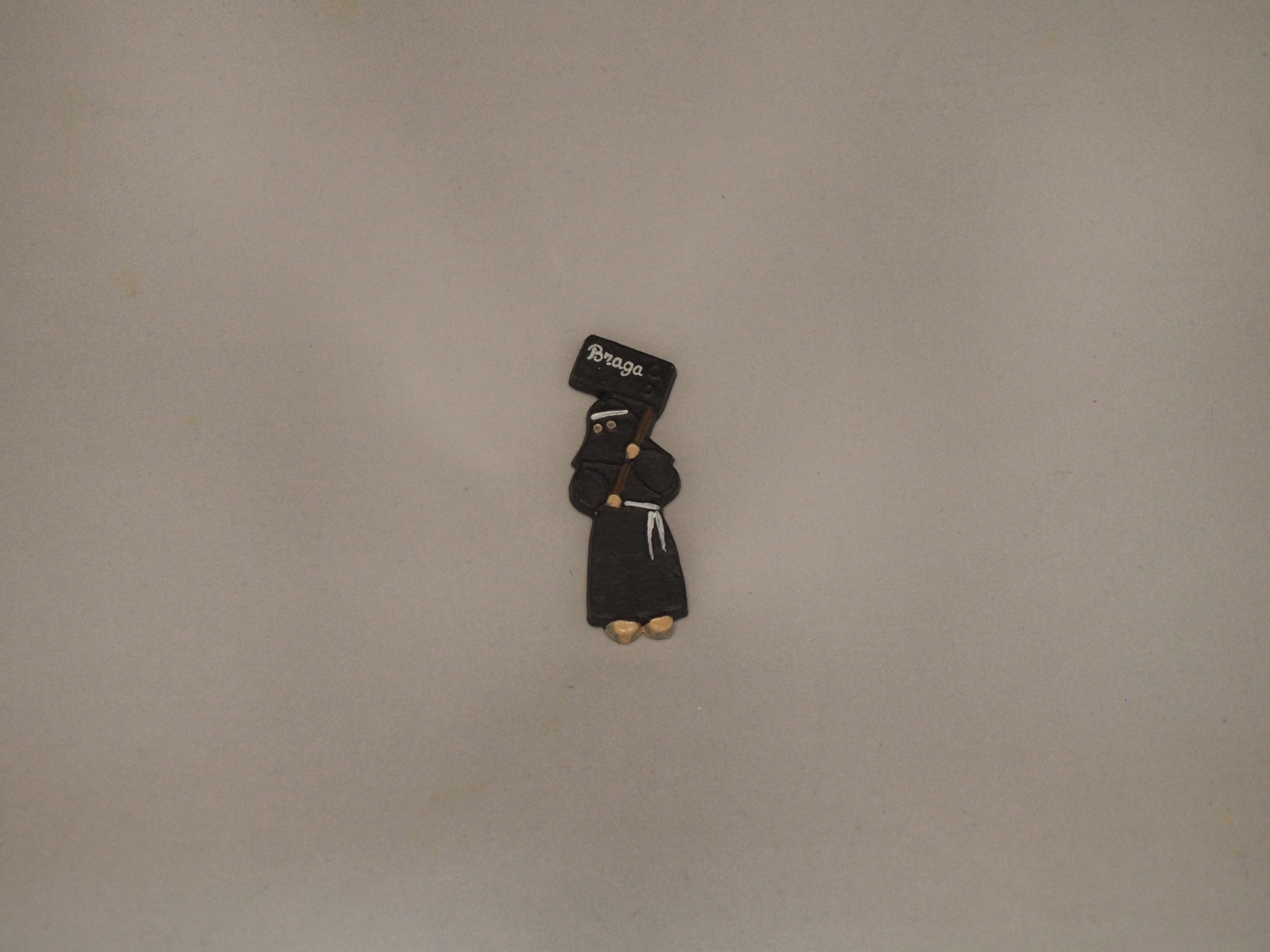Pequeno boneco decorativo preto com placa 'BRAGA' numa superfície cinza