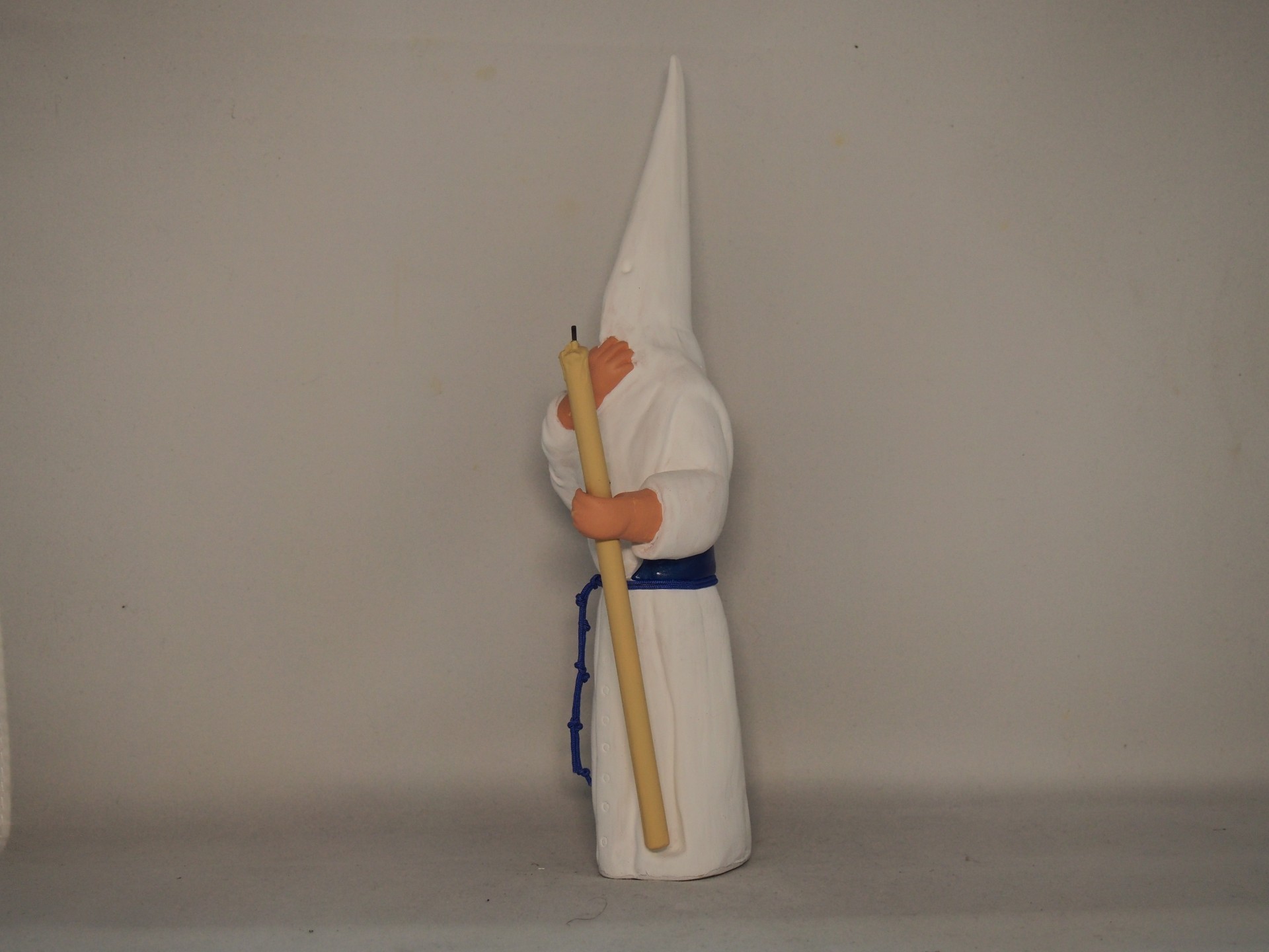 Figura decorativa com túnica branca e capuz, segurando vela