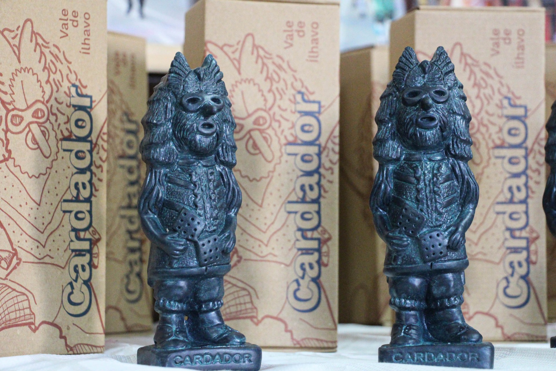 Duas estatuetas escuras de lobo antropomórfico com caixas ao fundo da marca Candador