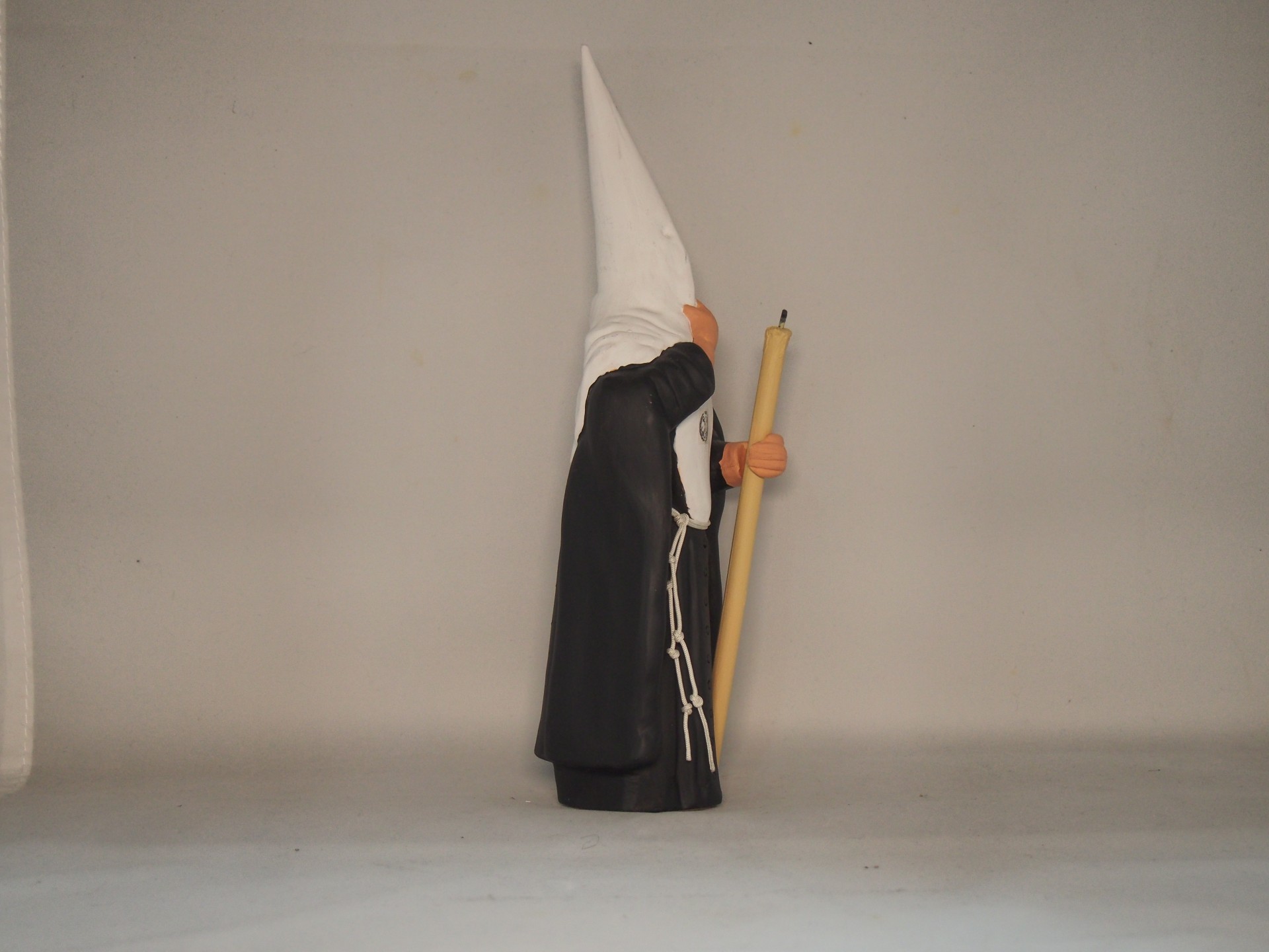 Estatueta com túnica preta e capuz branco pontudo segurando bastão de madeira