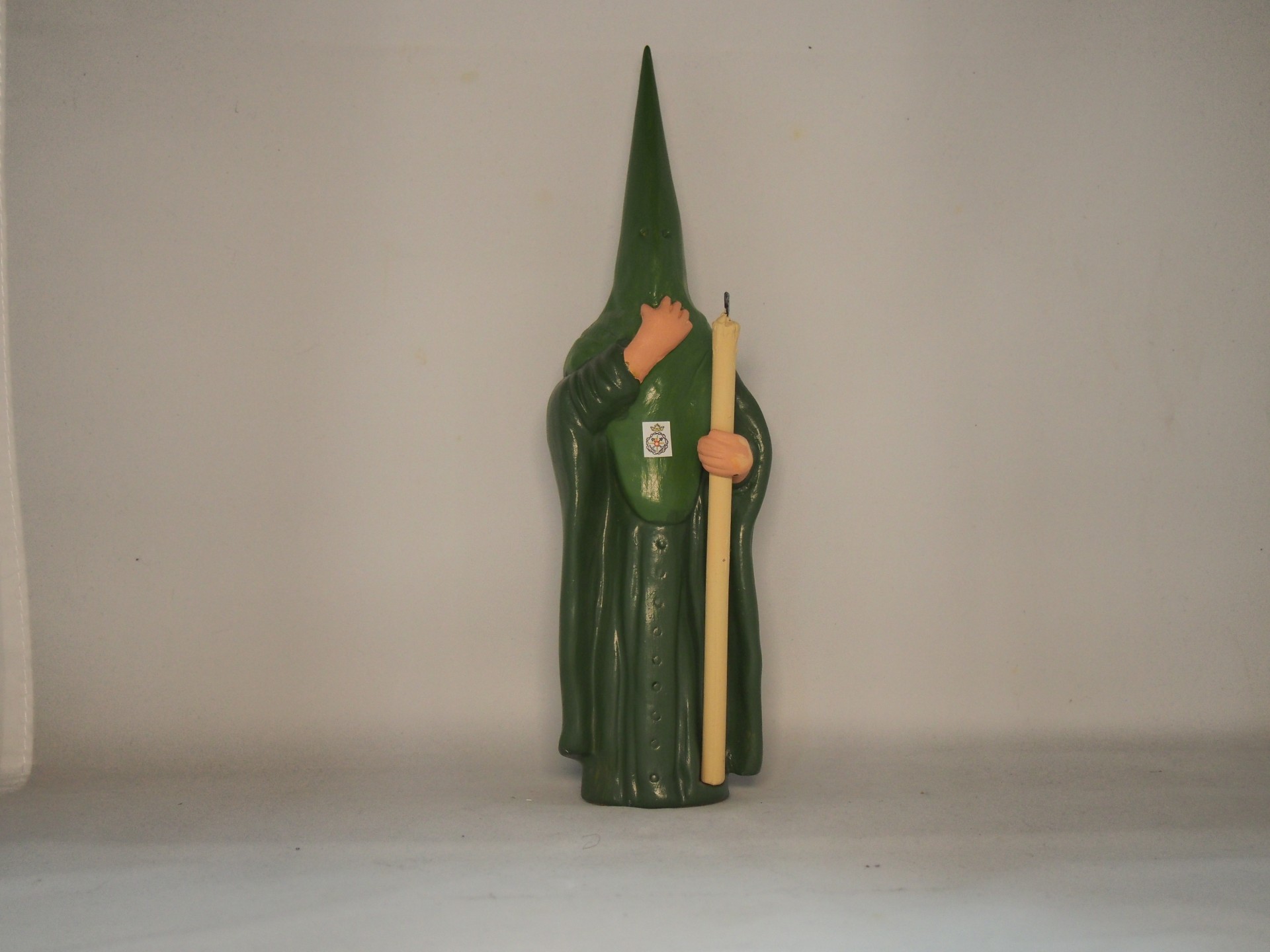 Estátua verde com capuz segurando vela amarela em fundo branco