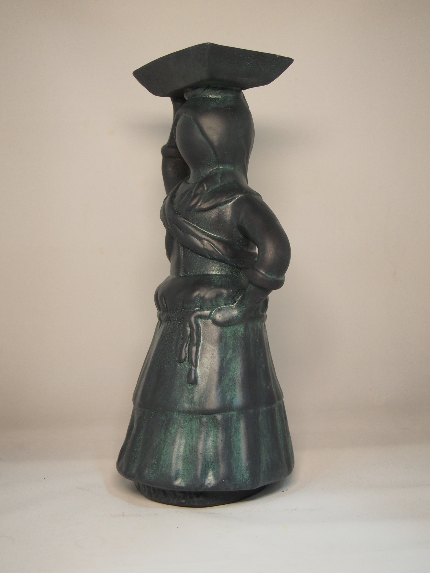 Estatueta cerâmica verde escuro com figura em traje tradicional e chapéu quadrado