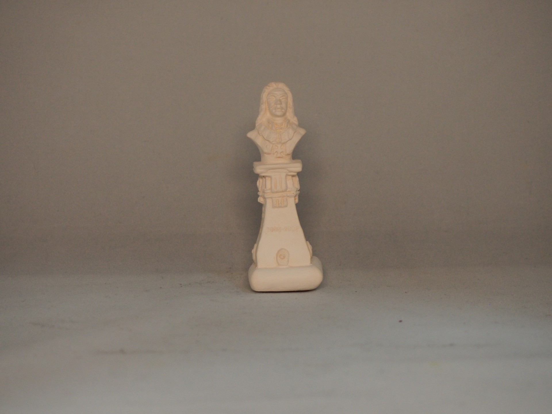 Figura decorativa bege claro com busto de mulher sobre base retangular num fundo cinzento