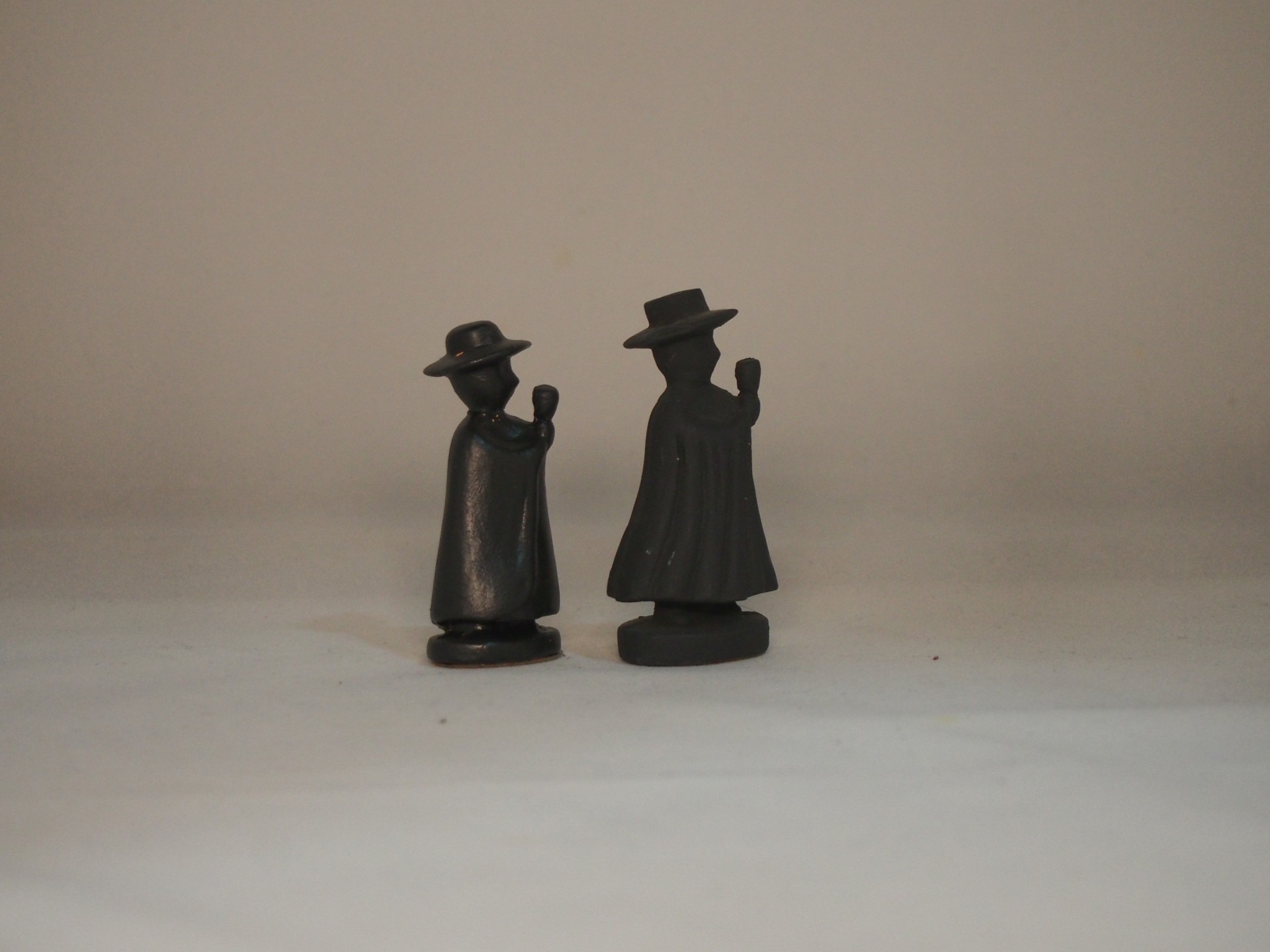 Duas figuras negras com chapéus e capas, vista traseira.