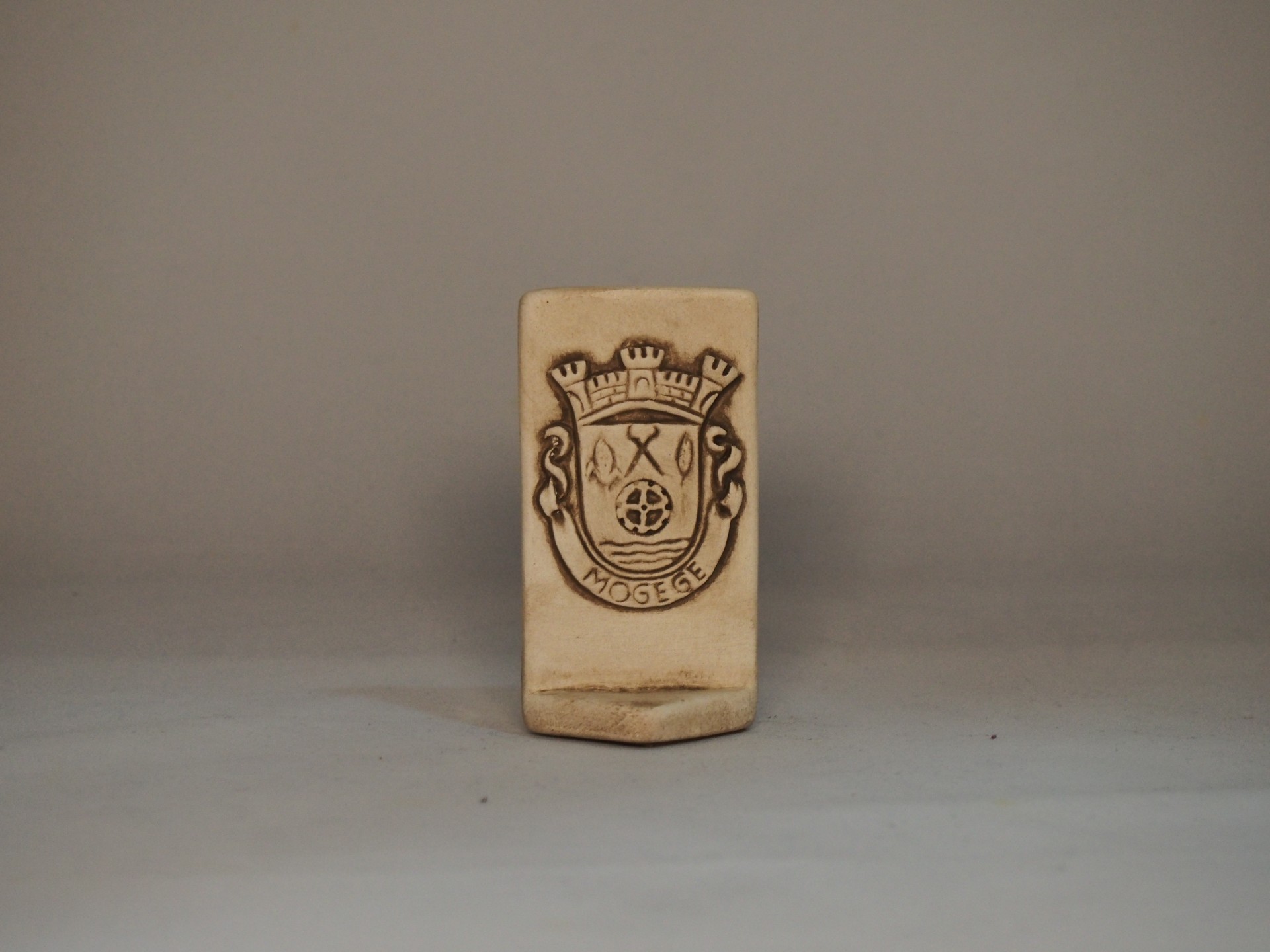 Produto de cerâmica bege com brasão gravado e texto 'MOSEGE'