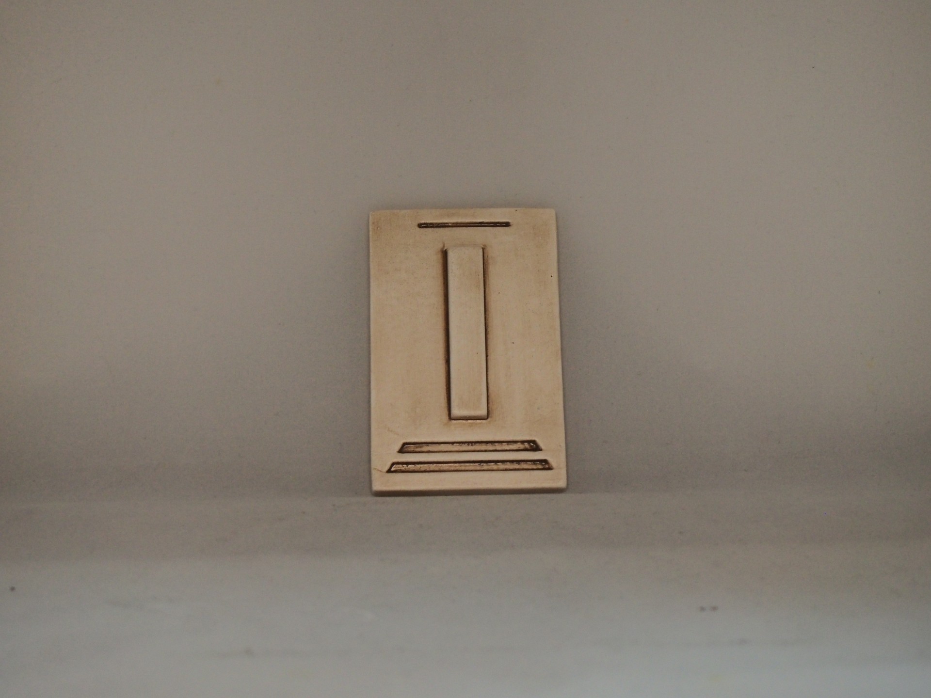 Placa decorativa castanha clara com relevo geométrico sobre fundo cinzento