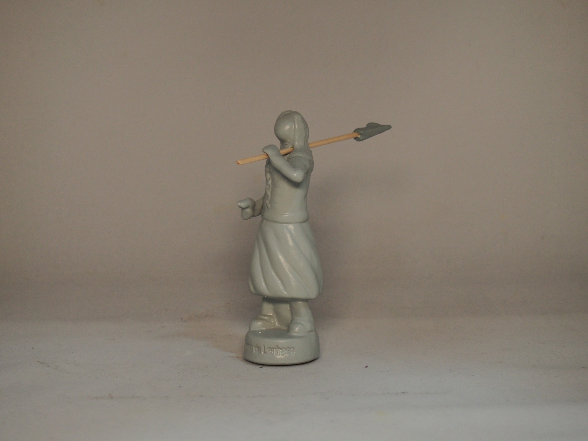 Figurina cinzenta de mulher segurando lança com ponta de flecha, sobre base redonda