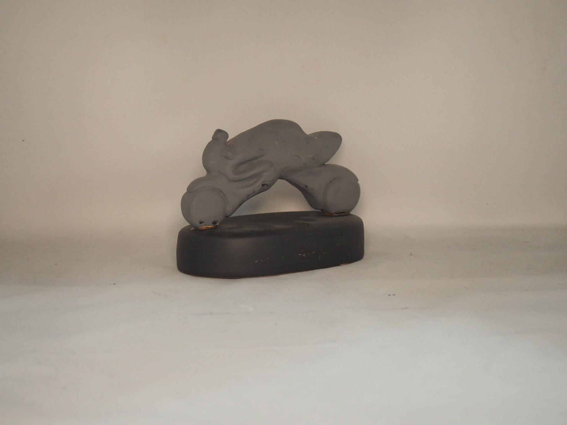 Estátua de golfinho cinzenta num suporte negro sobre superfície branca