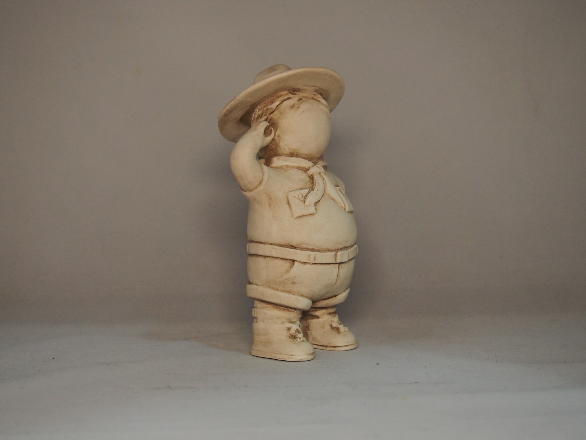 Estátua de criança em resina bege com chapéu e roupa, em pose de saudação