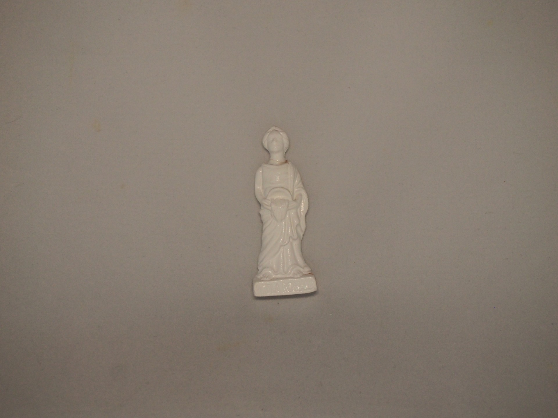 Estatueta branca de mulher com vestido e chapéu em superfície cinzenta