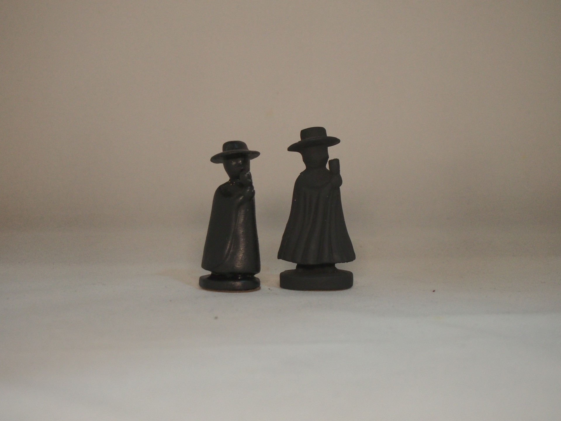 Duas miniaturas pretas de figuras humanas com capa e chapéu