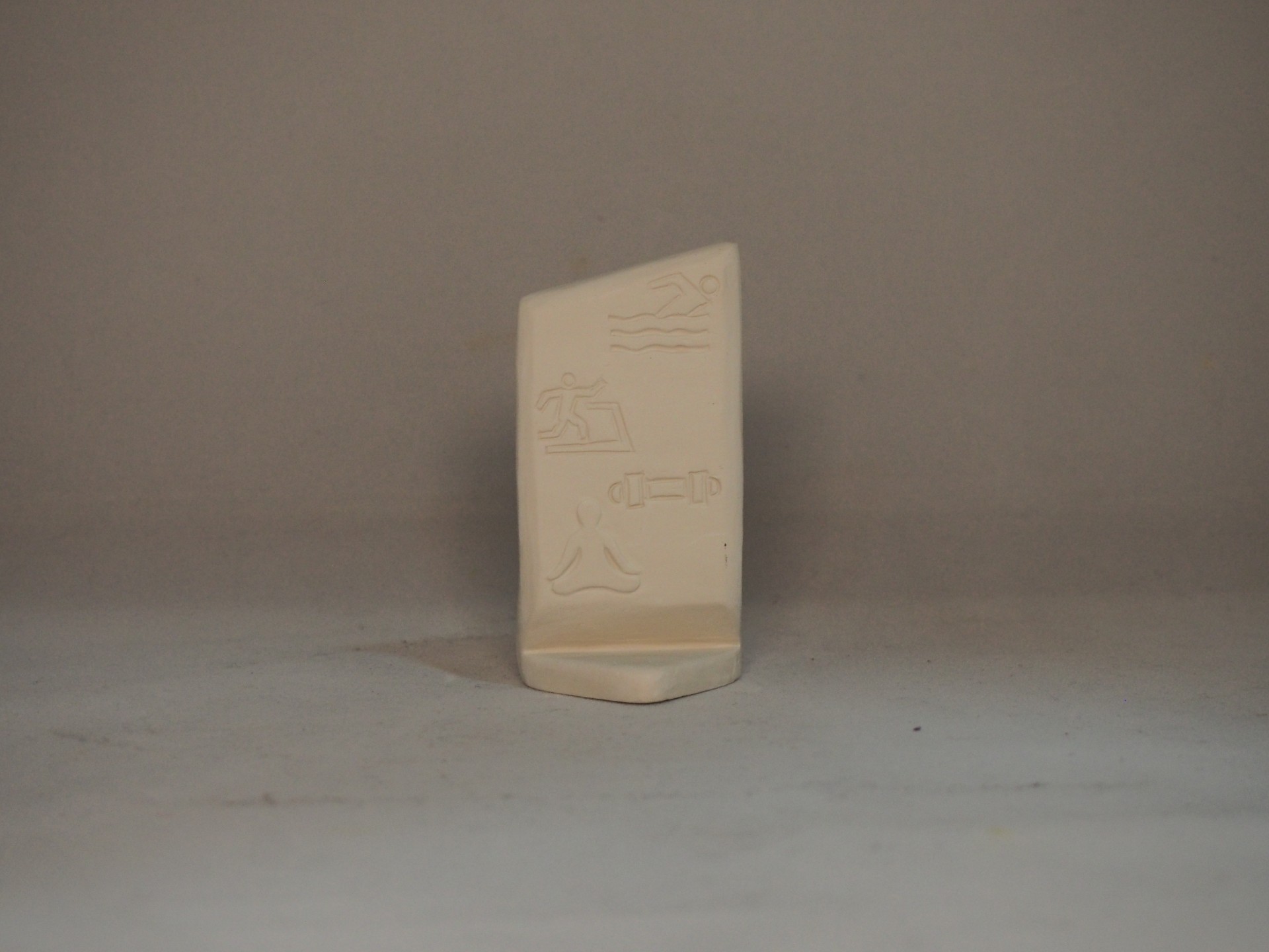 Estatueta bege com símbolos gravados em relevo sobre fundo cinzento