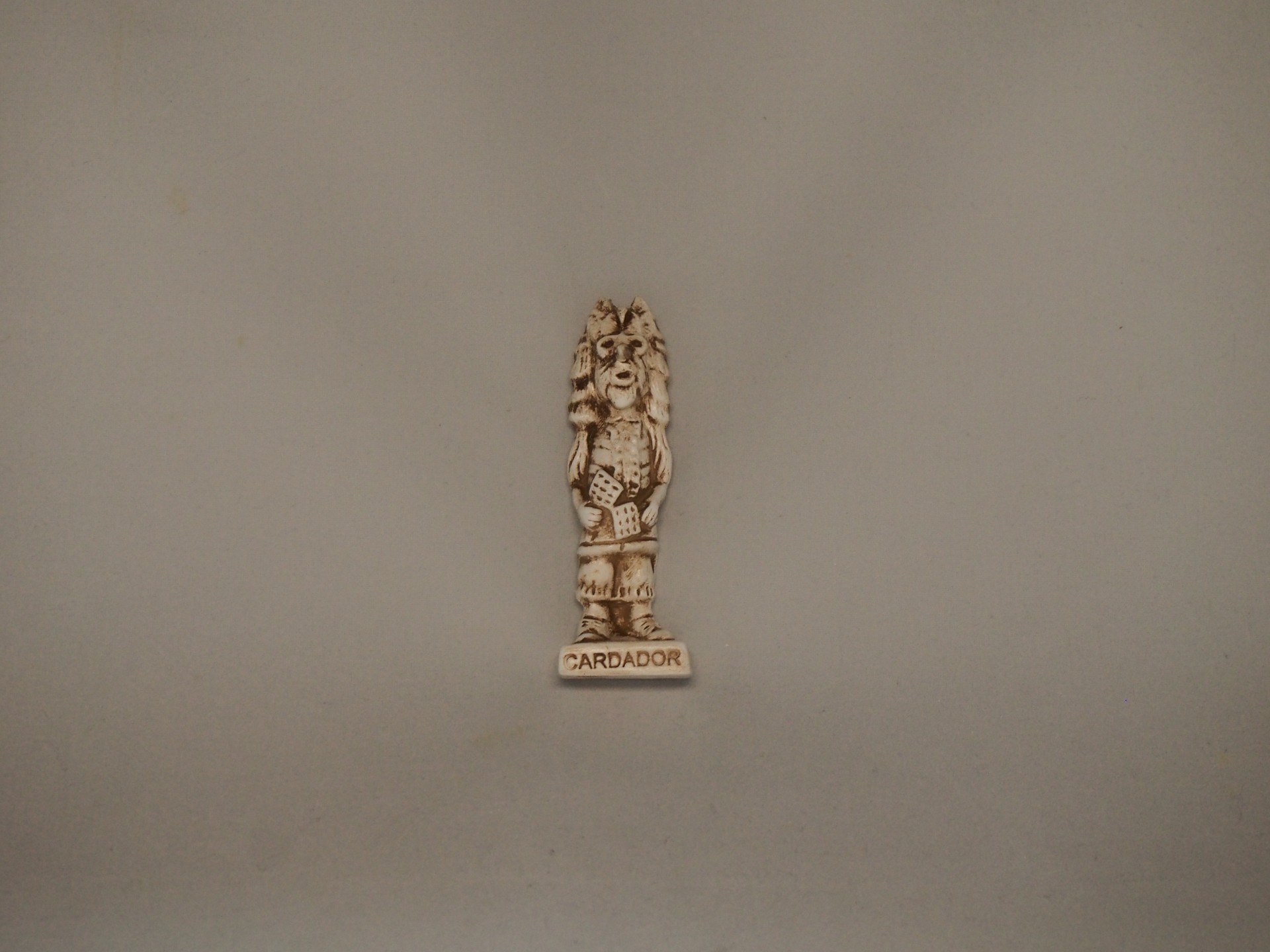 Estátua pequena bege com inscrição CARDADOR e figura estilizada