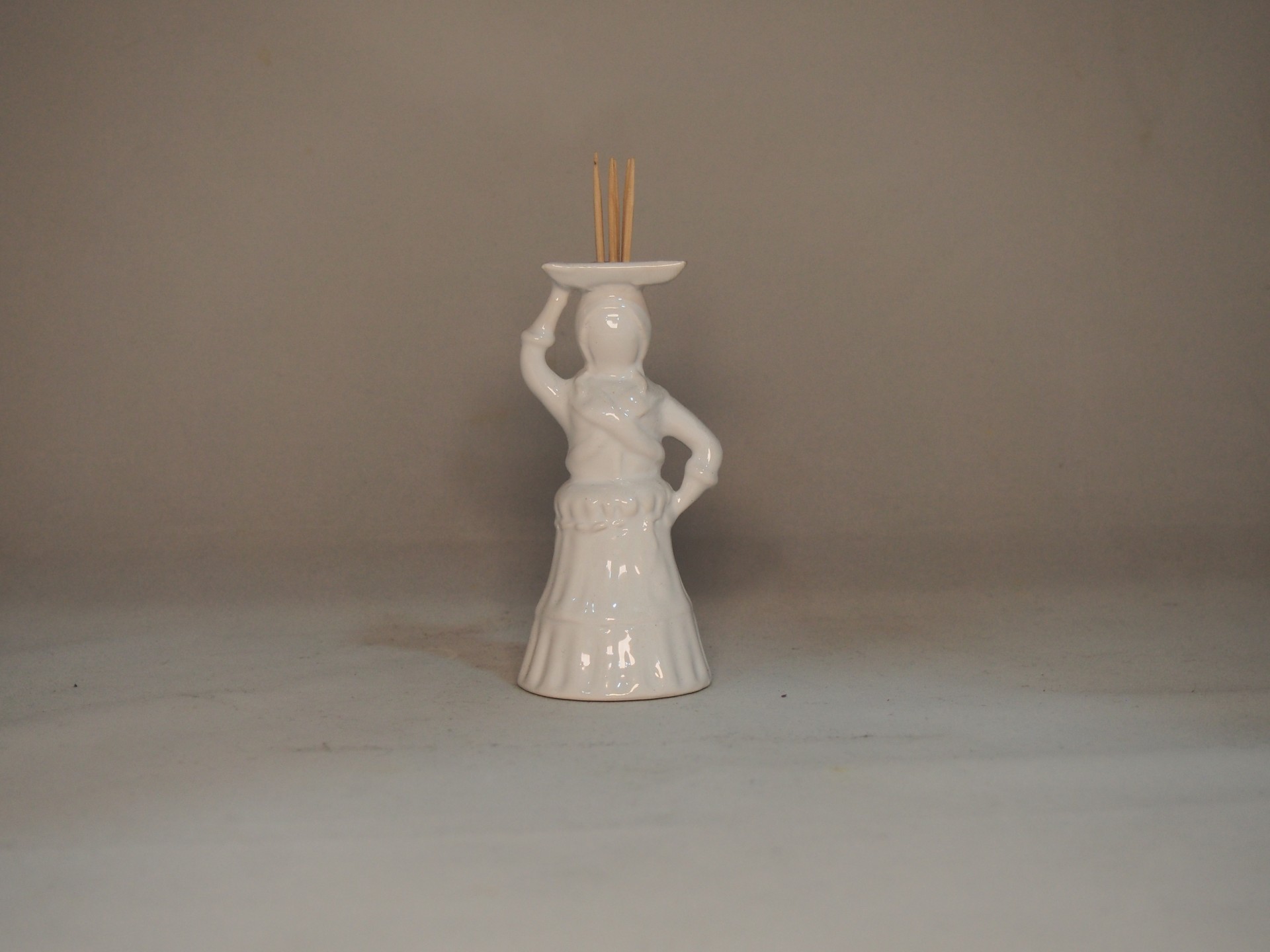 Figurinha decorativa em cerâmica branca com palitos de incenso.