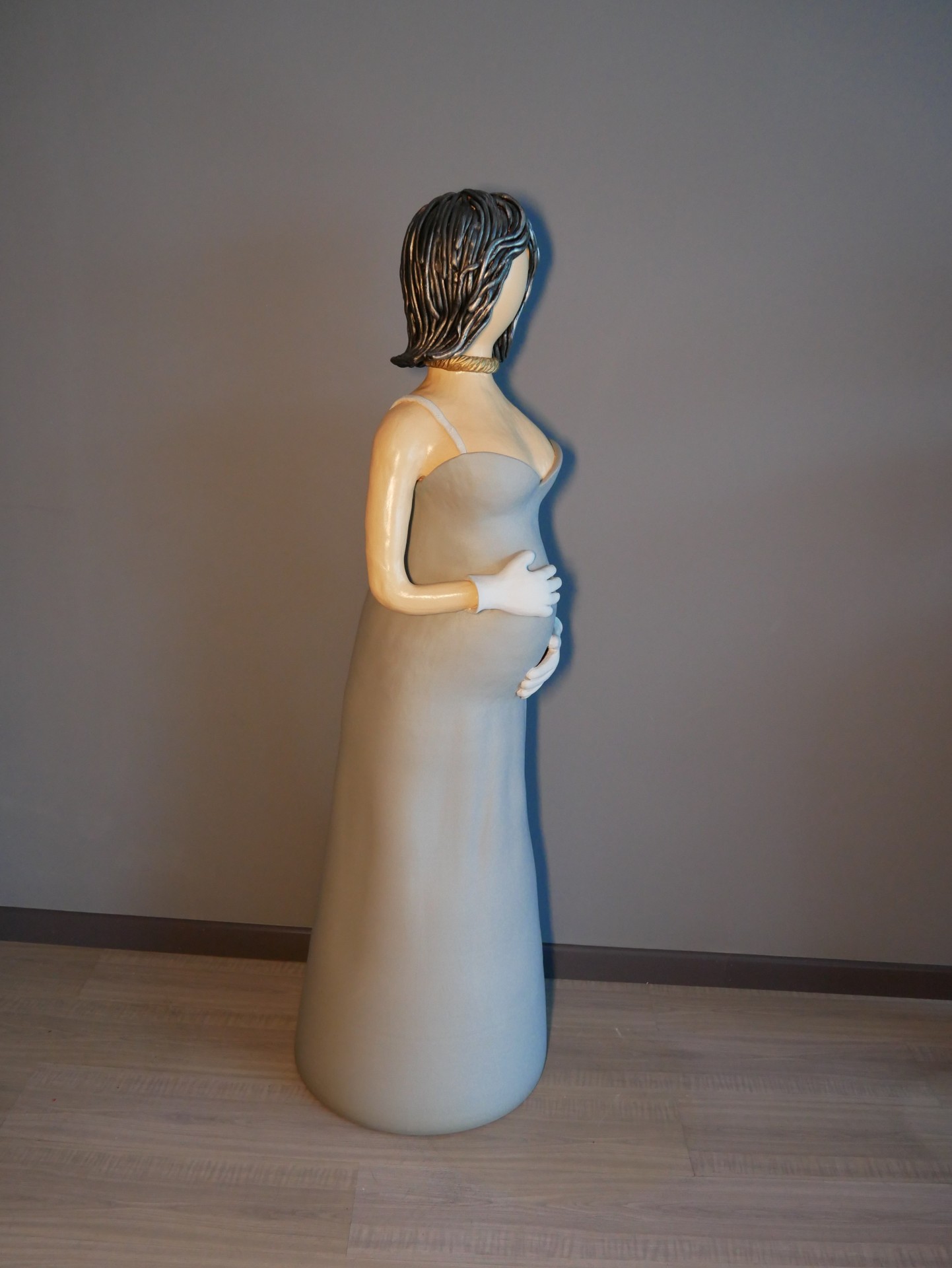 Estátua de mulher grávida em vestido cinza longe com cabelo castanho escuro