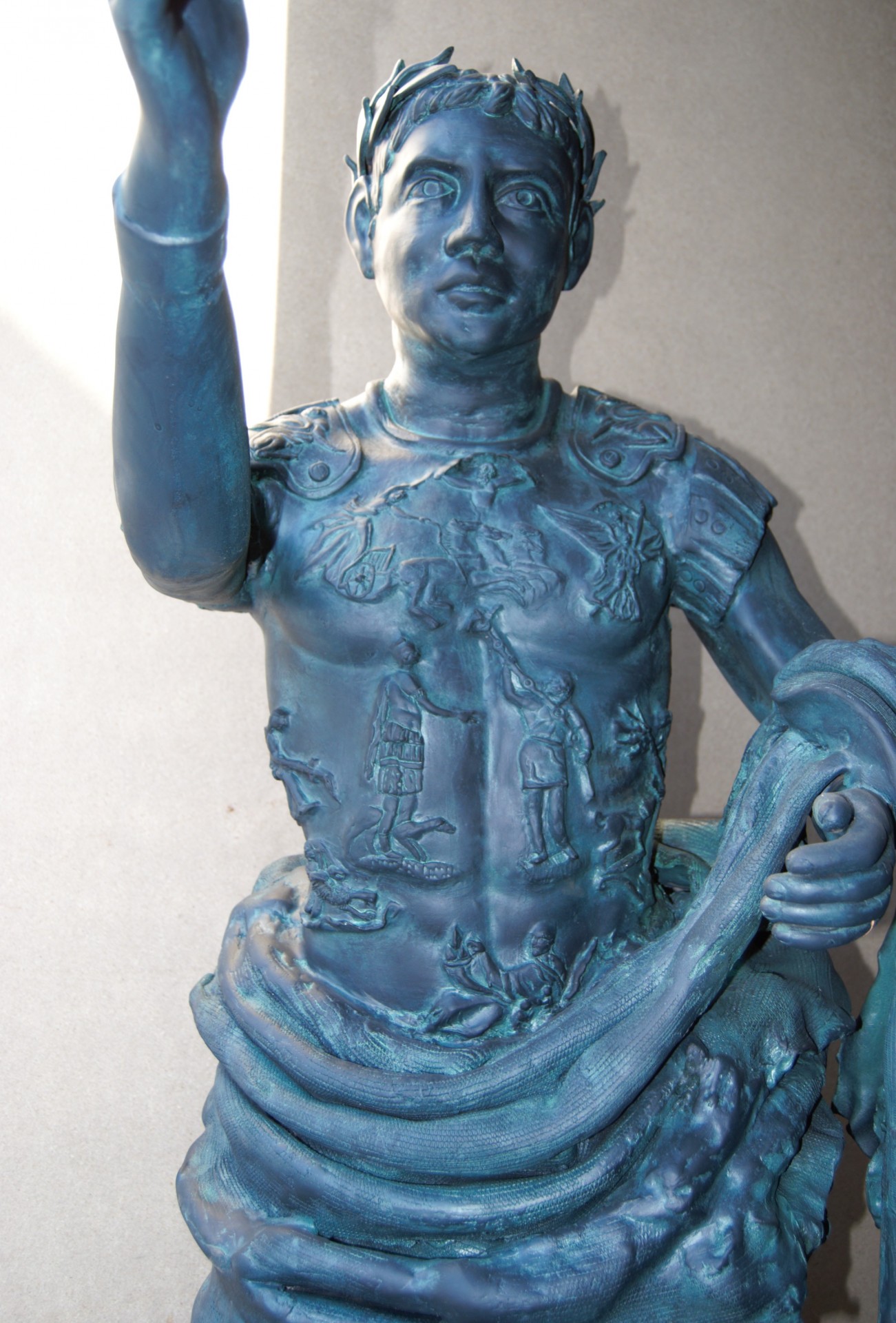 Estátua azul esverdeada de figura humana com armadura detalhada em fundo neutro