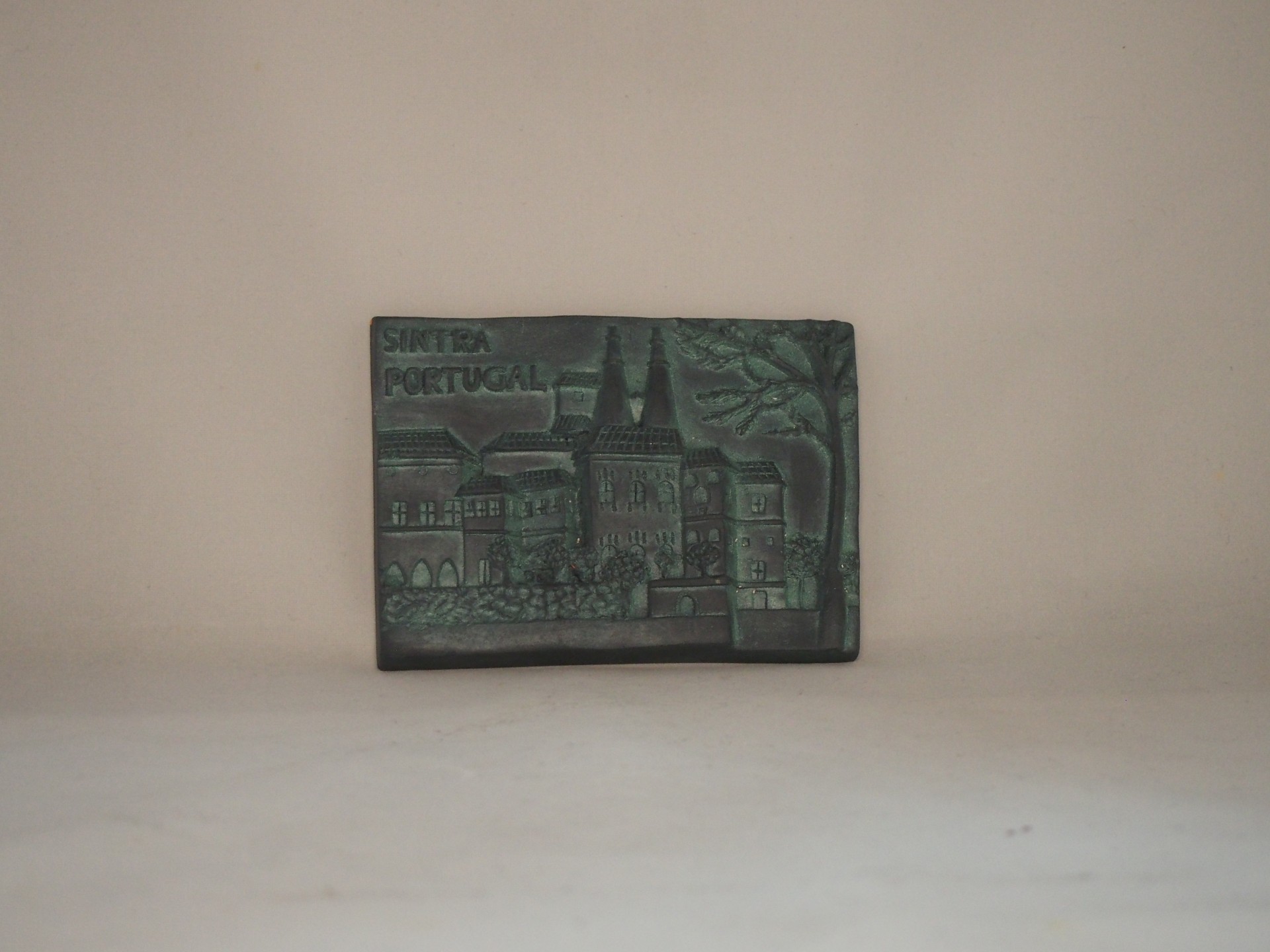 Magnético de cortiça verde escuro com relevo de edifício e árvore.