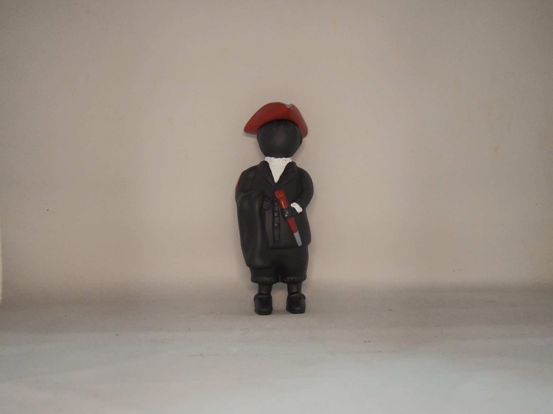 Figura decorativa preta com roupa e boina vermelha em fundo claro
