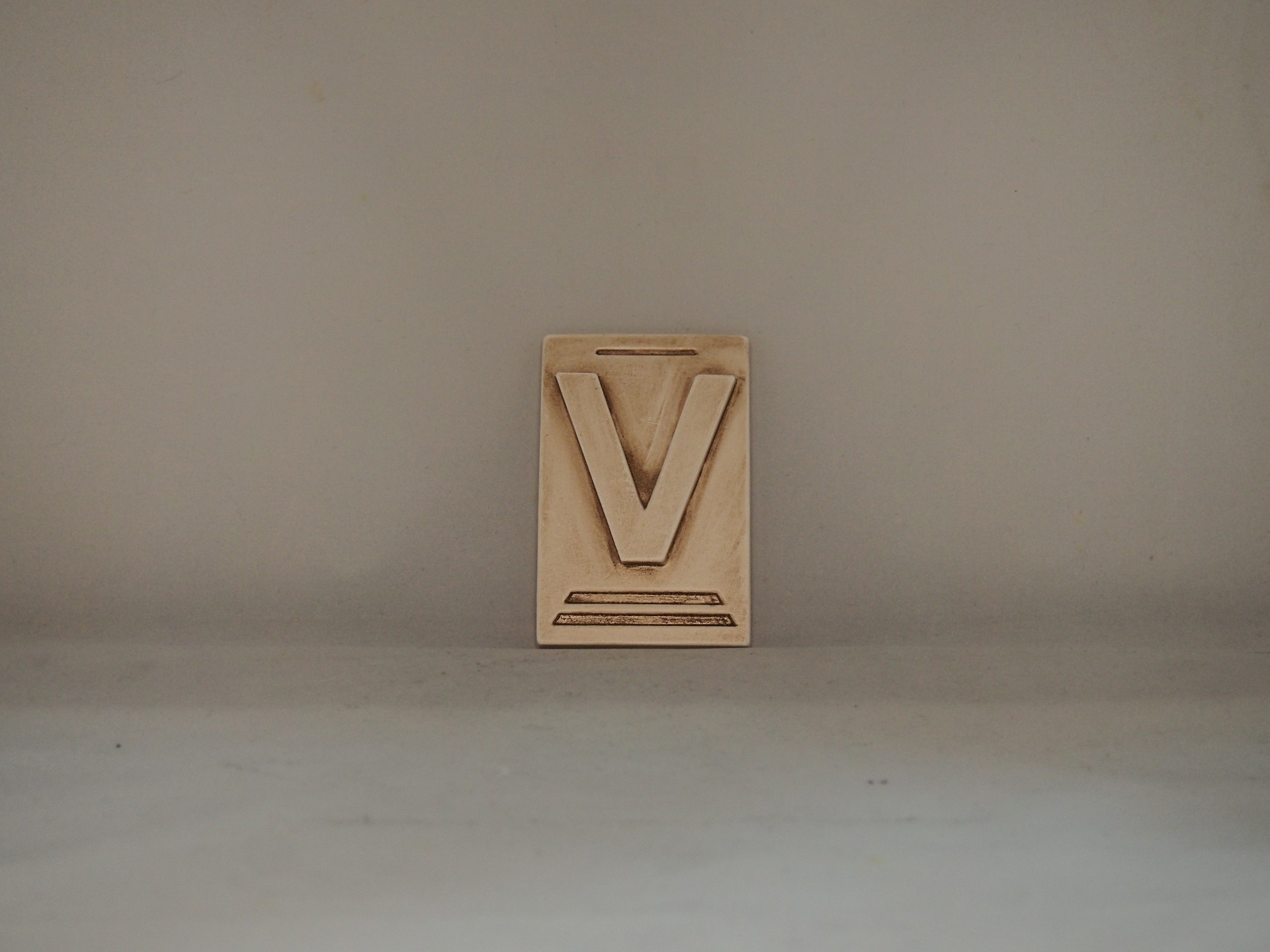 objeto decorativo em madeira clara com letra V em relevo
