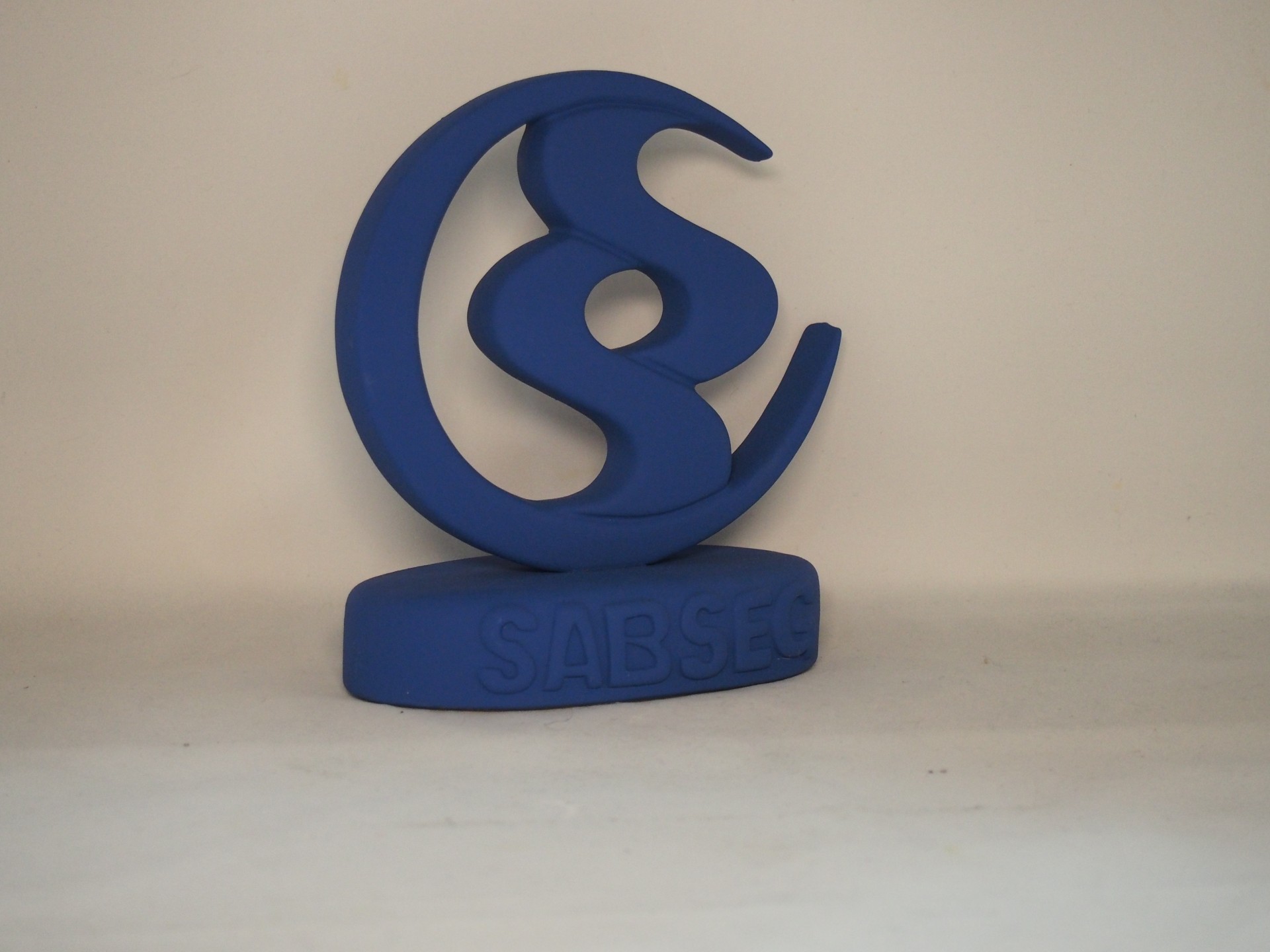 Escultura/troféu azul com gravação SABSEG sobre superfície branca