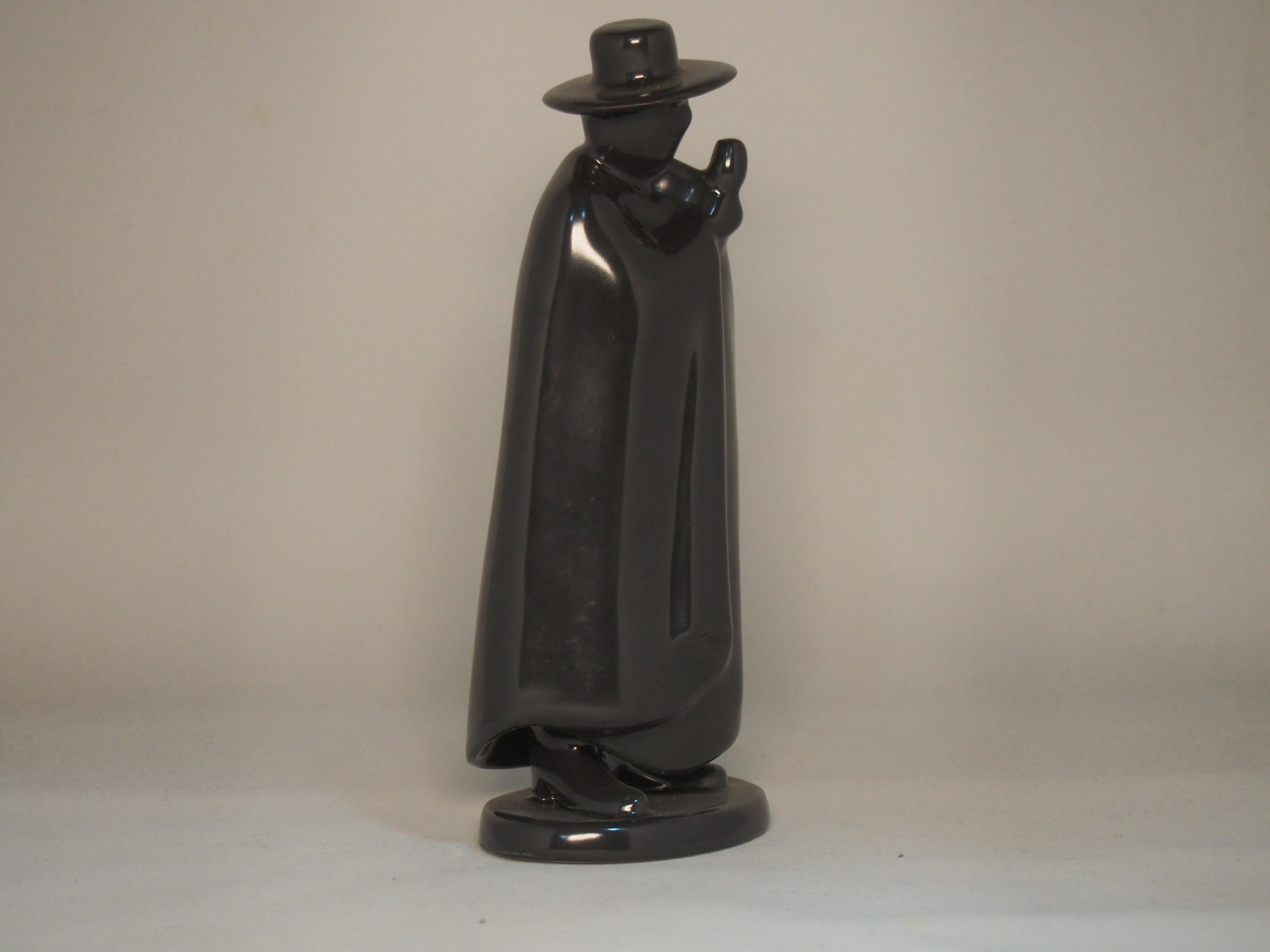 Estátua preta brilhante de figura masculina com capa e chapéu.