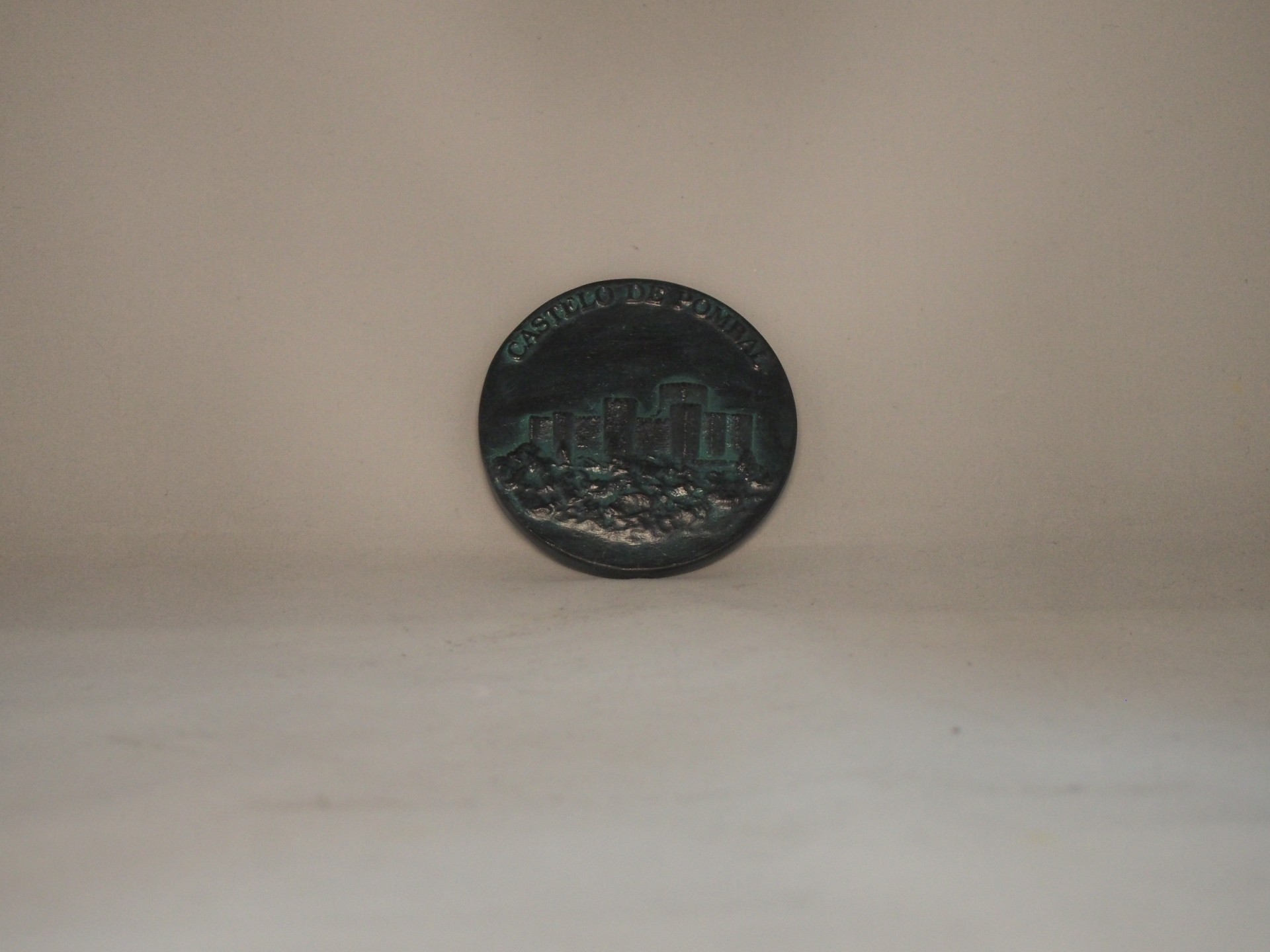 Moeda metálica escura com relevo de edifícios sobre fundo claro