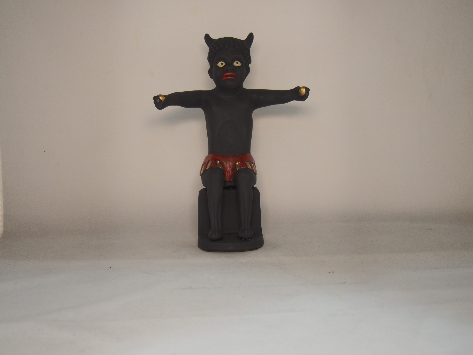 Figura esculpida negra com orelhas pontiagudas e calções vermelhos numa base preta