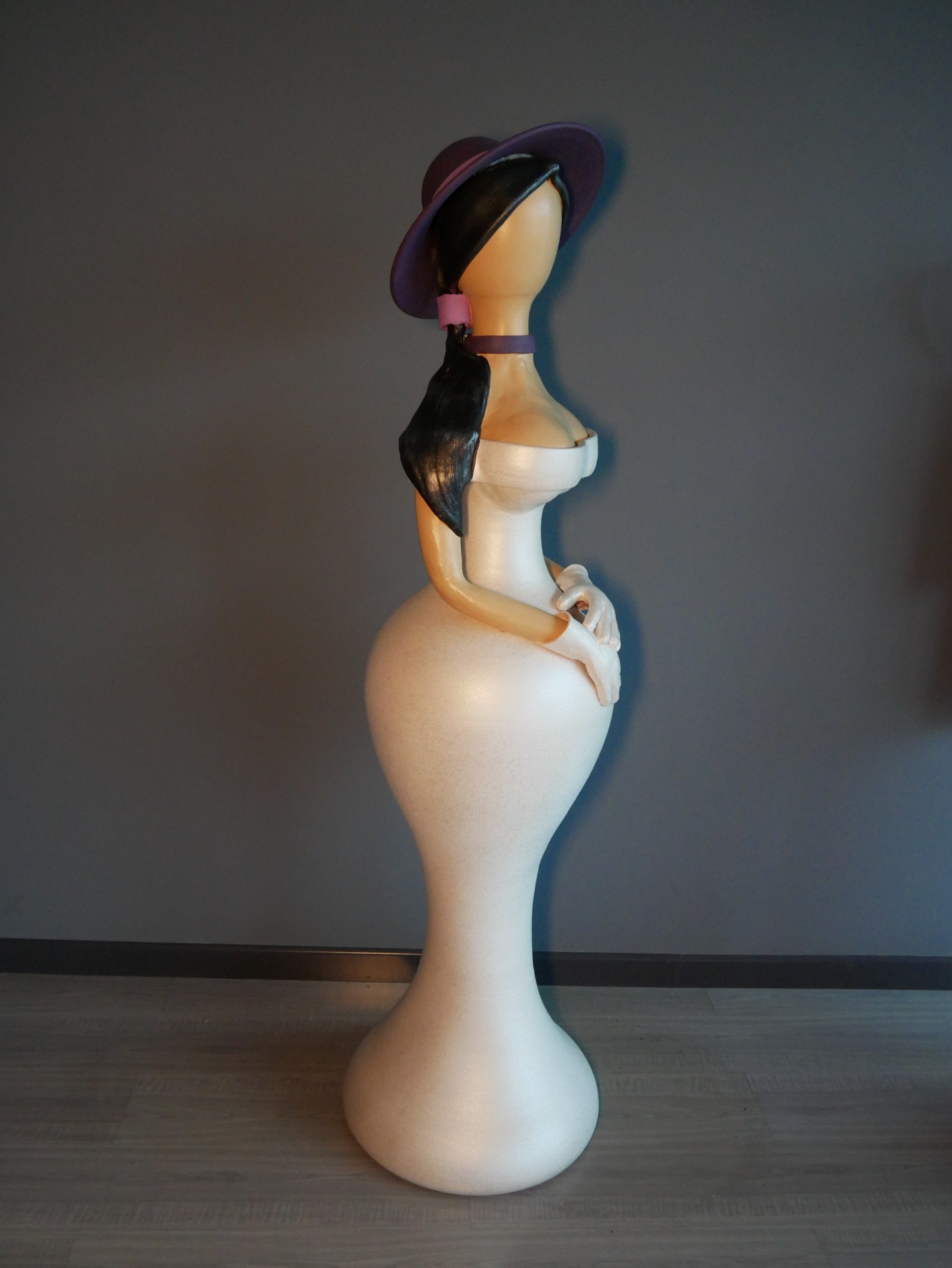 Estátua feminina estilizada com vestido branco e chapéu roxo